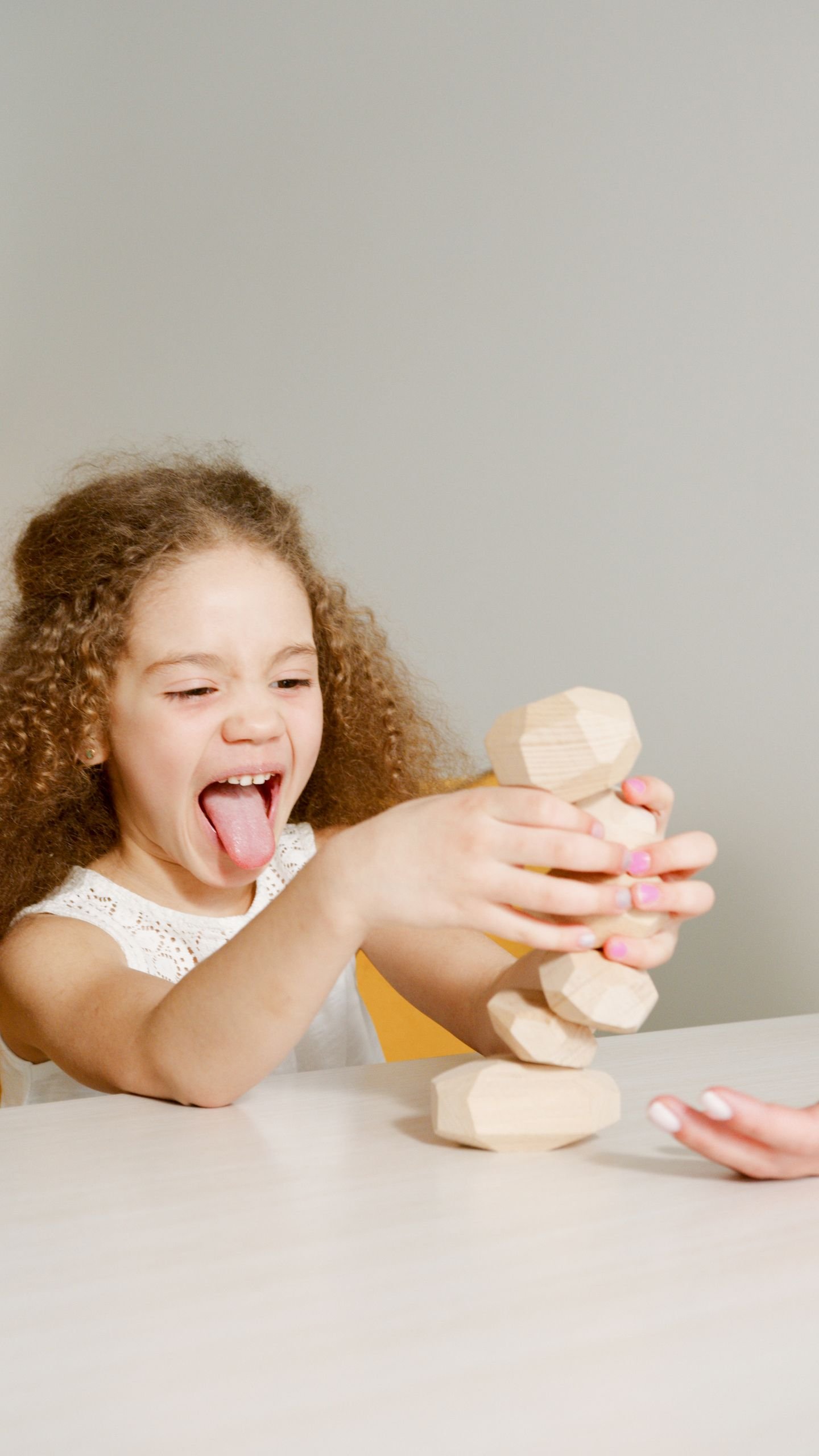 A happy child with curly hair plays with wooden blocks, enjoying a fun game.