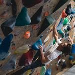 A young man engages in a challenging bouldering activity on a vibrant indoor climbing wall.