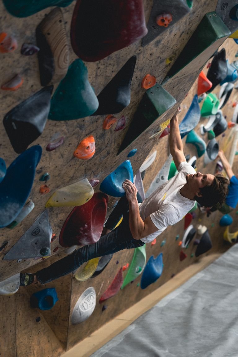 A young man engages in a challenging bouldering activity on a vibrant indoor climbing wall.