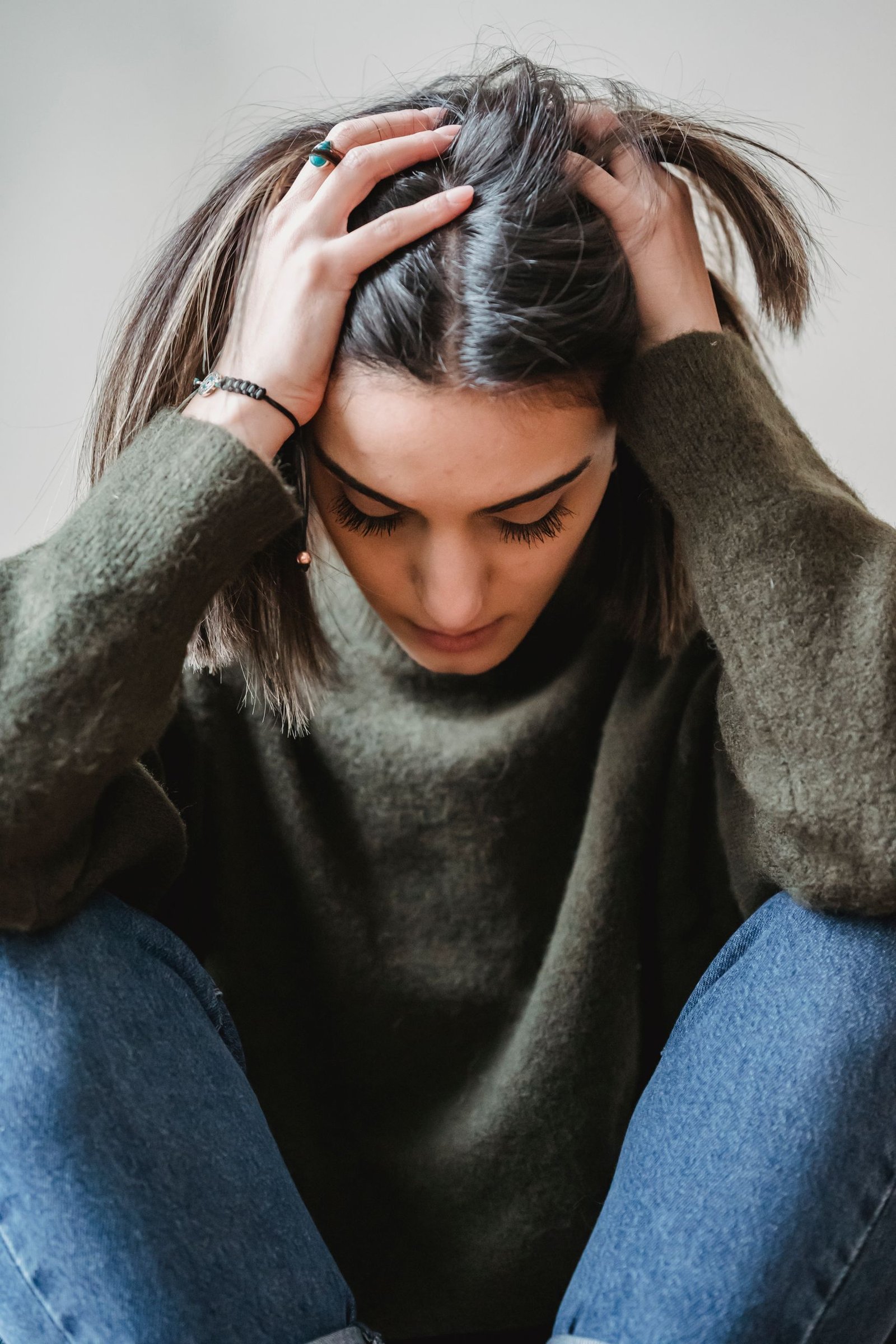 Desperate female in casual clothes touching head while sitting near white wall with bent legs in light room at home